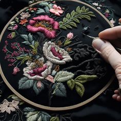 a person is stitching flowers on a black cloth with a pair of scissors in their hand