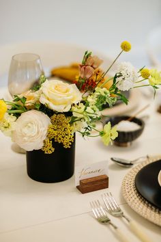 a table set with plates, silverware and flowers in a black vase on it