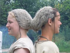 two people with long hair and braids standing next to each other in front of trees