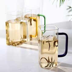 three glasses filled with liquid sitting next to each other on a white counter top in front of a potted plant