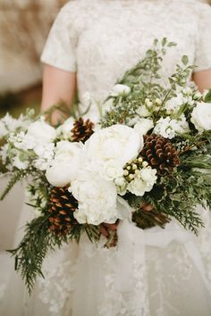 a bride holding a bouquet of white flowers and pine cones