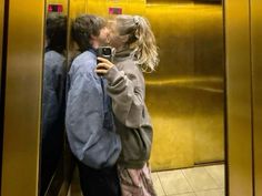 a man and woman kissing while standing in front of an elevator with their cell phone