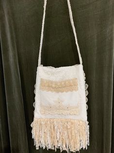 a white purse with fringes hanging on a green curtained wall in front of a black background