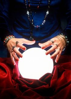 a woman holding a glowing ball in her hands on a red cloth covered tablecloth