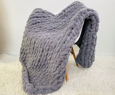 a gray blanket sitting on top of a wooden chair next to a white carpeted floor