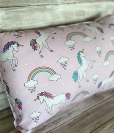 a pink pillow with unicorns and rainbows all over it on a wooden bench