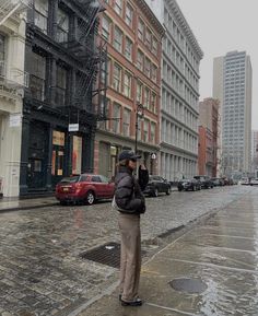 a woman standing on the side of a street talking on a cell phone while holding an umbrella