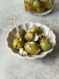 a white bowl filled with green olives covered in feta cheese and wooden skewers