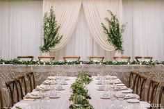 a long table with place settings and greenery on the wall in front of it