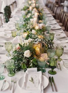 a long table is set with green and white plates, silverware, candles and greenery