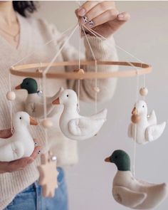 a woman is holding a mobile with ducks and geese hanging from it's sides