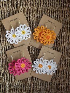 four crocheted flower earrings sitting on top of a wicker table next to each other