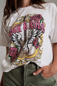 Embrace the spirit of rock and roll with our Vintage Rock and Roll Print T-Shirt in White. Crafted from 100% cotton, this tee offers not only style but also a comfortable fit. The model, with measurements 33-24-35 and a height of 5'8'', confidently sports size U, ensuring a true-to-size fit. This t-shirt boasts a regular fit and full length, making it a versatile addition to your wardrobe. The classic crew neckline and short sleeves provide a timeless look, while the relaxed fit ensures all-day White Rock And Roll Graphic Print Top, White Graphic Rock And Roll T-shirt, Graphic Print Rock And Roll T-shirt, Rock And Roll Cotton T-shirt With Band Logo, Rock And Roll Cotton Graphic T-shirt, Vintage Rock, Vintage Inspired Design, Boho Vibe, Comfy Tees