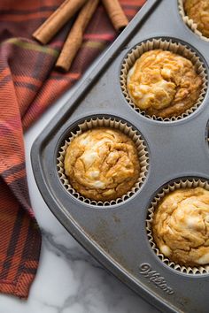 a muffin tin filled with orange cupcakes and cinnamon sticks