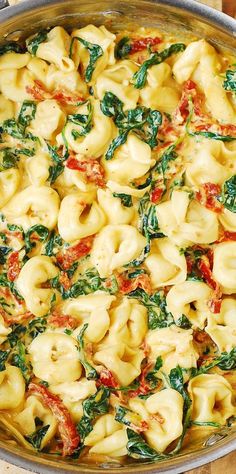 a pan filled with pasta and spinach on top of a wooden table next to utensils