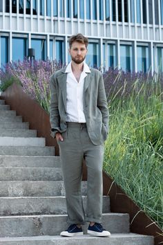 a man is standing on some steps in front of purple flowers and tall grass with his hands in his pockets