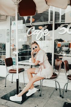 a woman sitting at a table talking on her cell phone in front of a cafe