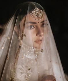 a woman wearing a veil with gold beads on her head and in the background is an image of a bride's face