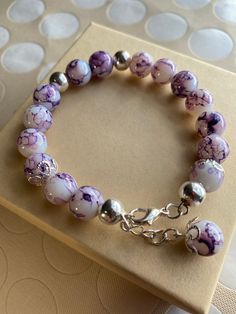 a purple and white bracelet with silver beads on a table next to polka dot circles