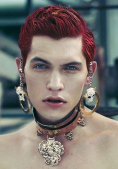 a young man with red hair wearing large earrings and necklaces on his neck is staring at the camera