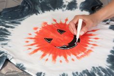 a person is drawing on a tie - dyed t - shirt with an orange smiley face