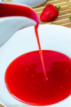 a red liquid being poured into a white bowl with strawberries on the table next to it