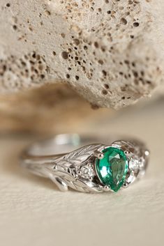 a close up of a ring with a green stone on it's side and a rock in the background