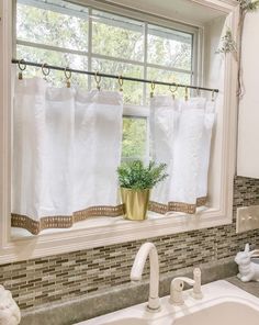 a kitchen sink under a window with white towels hanging from it's rod, and a potted plant in the window sill