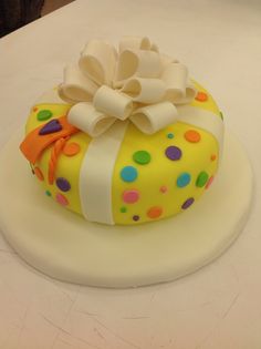 a yellow cake with polka dots and a big bow on it's top is sitting on a table