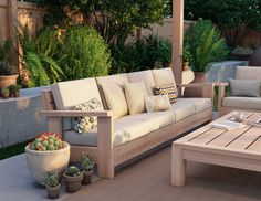 a couch and coffee table on a patio with potted plants in the back ground