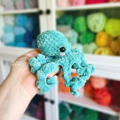 a hand holding an octopus stuffed animal in front of a shelf with crochet balls