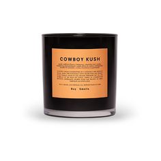 a black candle with an orange label on the top and bottom, sitting in front of a white background