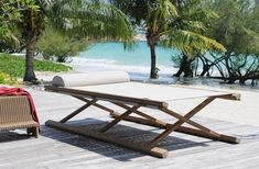 an outdoor lounge chair on a wooden deck near the water and palm trees in the background