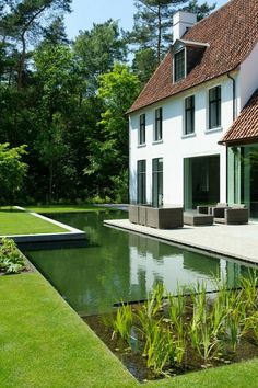 a house with a pond in front of it next to a lush green yard and trees