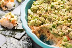 a blue bowl filled with food next to crackers and sushi rolls on top of a table