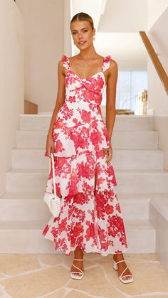 a woman in a red and white floral print dress standing on stairs with her handbag