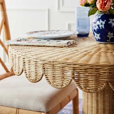 a wicker table with plates and flowers on it, next to a blue vase