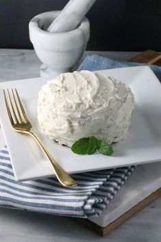 a white plate topped with a cake covered in frosting next to a knife and fork