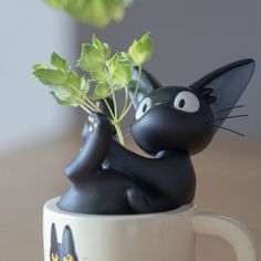 a black cat figurine sitting on top of a coffee cup with a plant in it