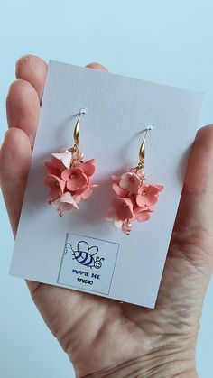 a pair of earrings with pink flowers hanging from it's earwires in front of a white card