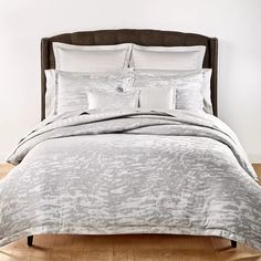 a bed with white and grey comforters in a bedroom setting on hardwood flooring