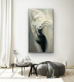 an abstract painting hangs on the wall above a round coffee table in a white living room