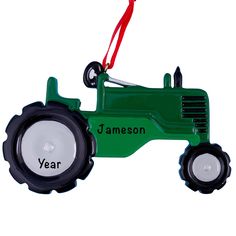 a green tractor ornament hanging from a red ribbon on a white background with the words, year