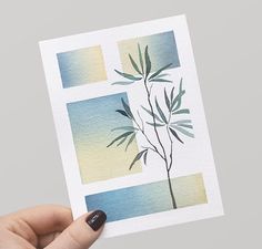 a hand holding up a piece of paper with watercolor painting on it and a plant in the middle