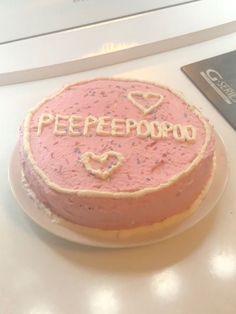 a pink cake with the word peepobo on it sitting on a table next to a laptop