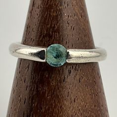 a close up of a ring with a stone on the top and bottom, sitting on a wooden stand