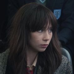 a woman with long hair sitting at a table in front of other people and looking off into the distance