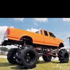 an orange truck with large tires parked in the grass