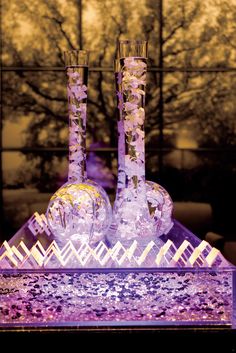 two glass vases sitting on top of a purple table