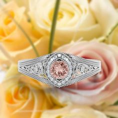 a pink diamond ring sitting on top of some white and yellow flowers with roses in the background